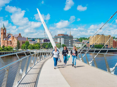 Young adults cross The Peace Bridge over River Foyle in downtown Derry, Northern Ireland, United Kingdom on a sunny day.