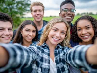 A group of multi-ethnic students taking a selfie outside.  They are dressed casually and having fun together in a group.