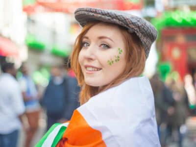 Smiling pretty red haired Irish girl with tweed hat, wrapped in the Irish flag and shamrocks painted on her face, Temple Bar, Dublin, Ireland.