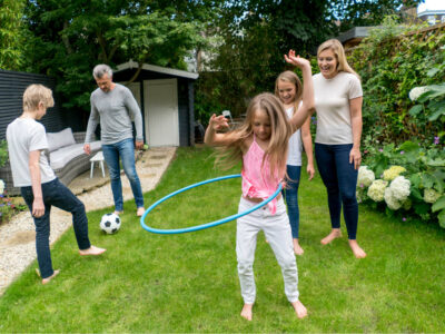 Happy family watching their girl playing with the hula hoop outdoors and enjoying the summer