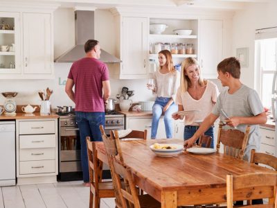 Family With Teenage Children Laying Table For Meal In Kitchen